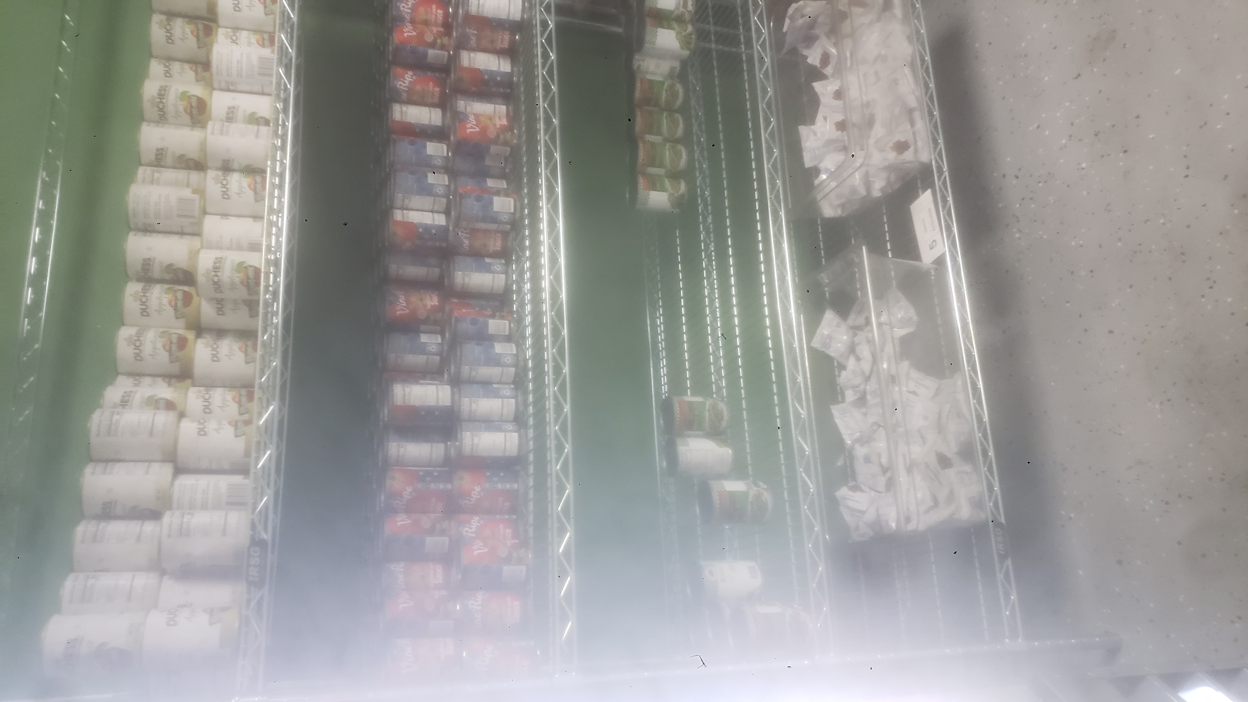 Canned applesauces, canned tomatoes sauces, packets of dried cranberries, and canned green beans on a four tier shelf.